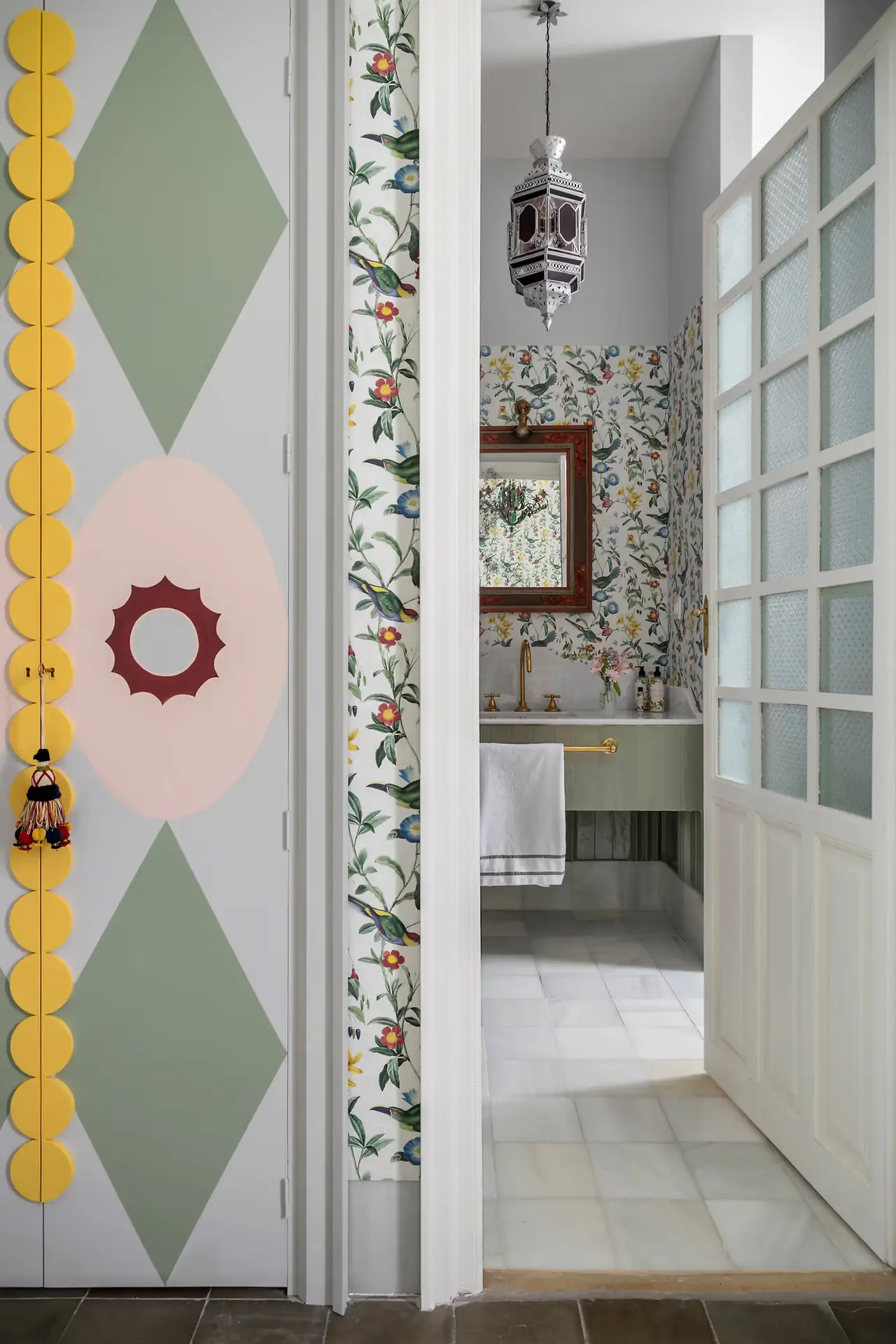 Vista desde una puerta abierta hacia un baño con paredes cubiertas de papel tapiz floral con aves, un lavabo