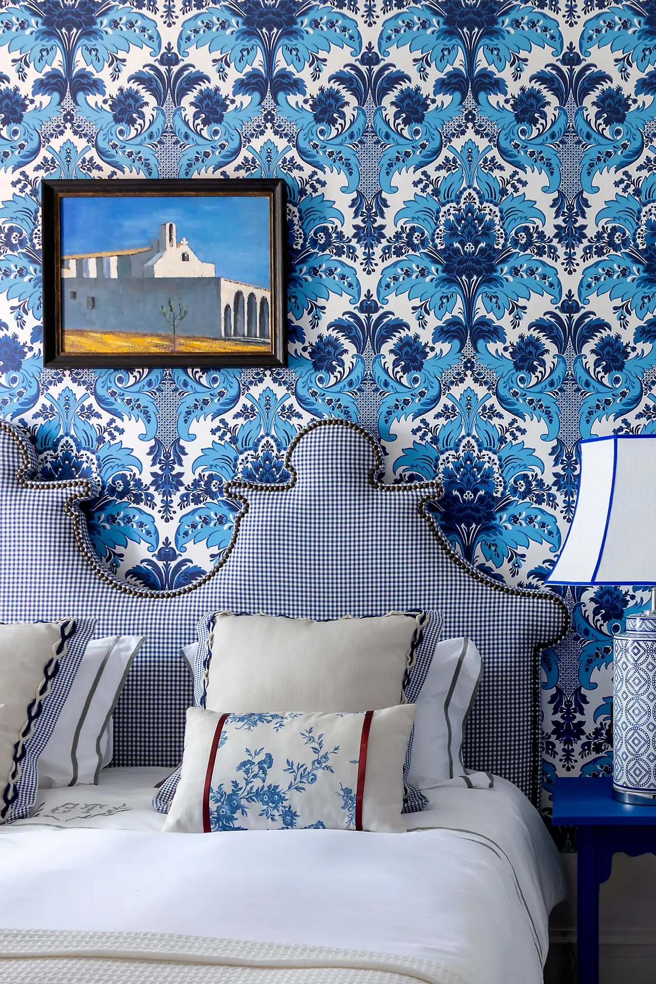Vista de una cama con cabecero tapizado en tela de cuadros azules y blancos, múltiples almohadas decorativas