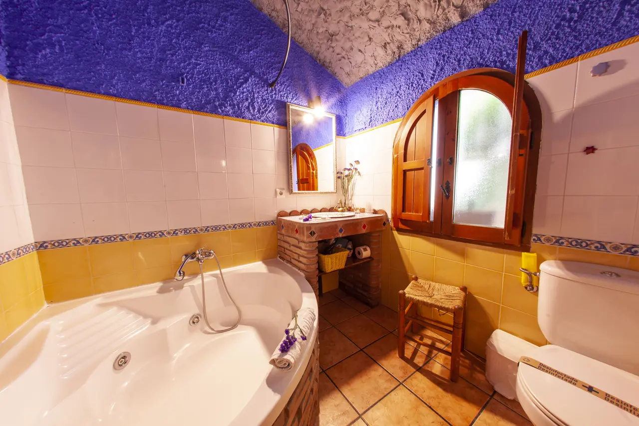 Jacuzzi blanco empotrado en una habitación con paredes de azulejos blancos y amarillos, techo abovedado azul y blanco