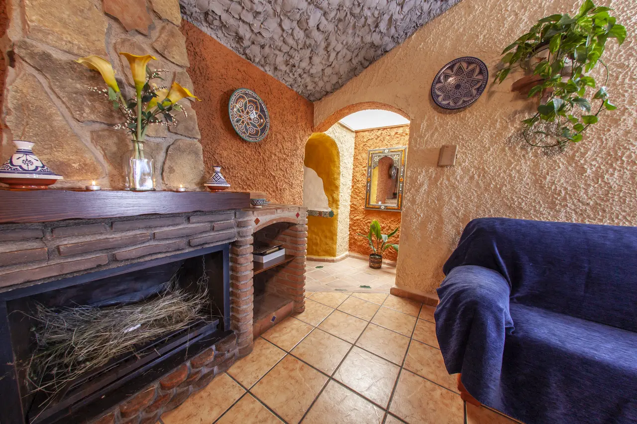 Interior de una habitación rústica con paredes de piedra y estuco, techo abovedado, chimenea de ladrillo con leña