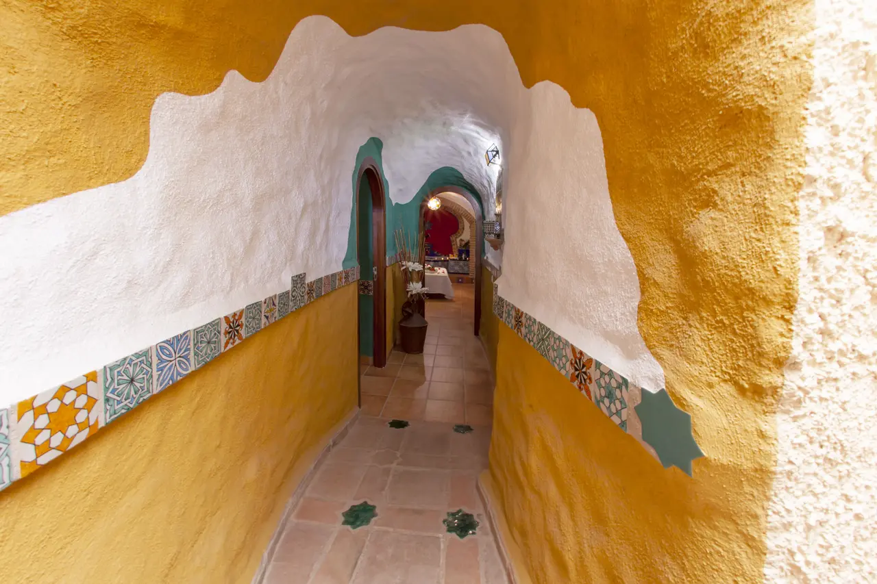 Pasillo abovedado en el interior de una cueva, con paredes pintadas en amarillo y blanco, zócalo de azulejos