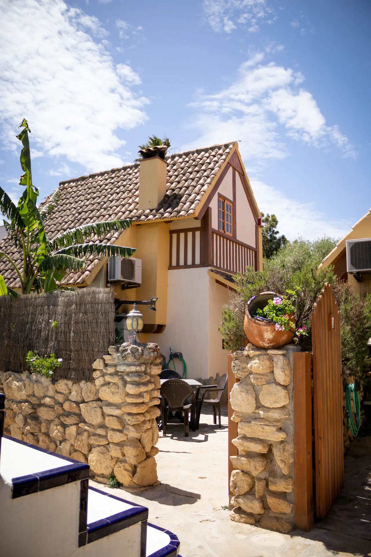 Vista exterior de una casa con fachada de dos tonos, tejado de tejas, chimenea y balcón de madera.