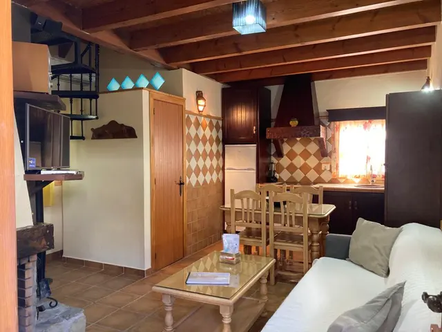 Interior de una sala de estar con sofá blanco, mesa de centro de madera, chimenea, zona de cocina al fondo
