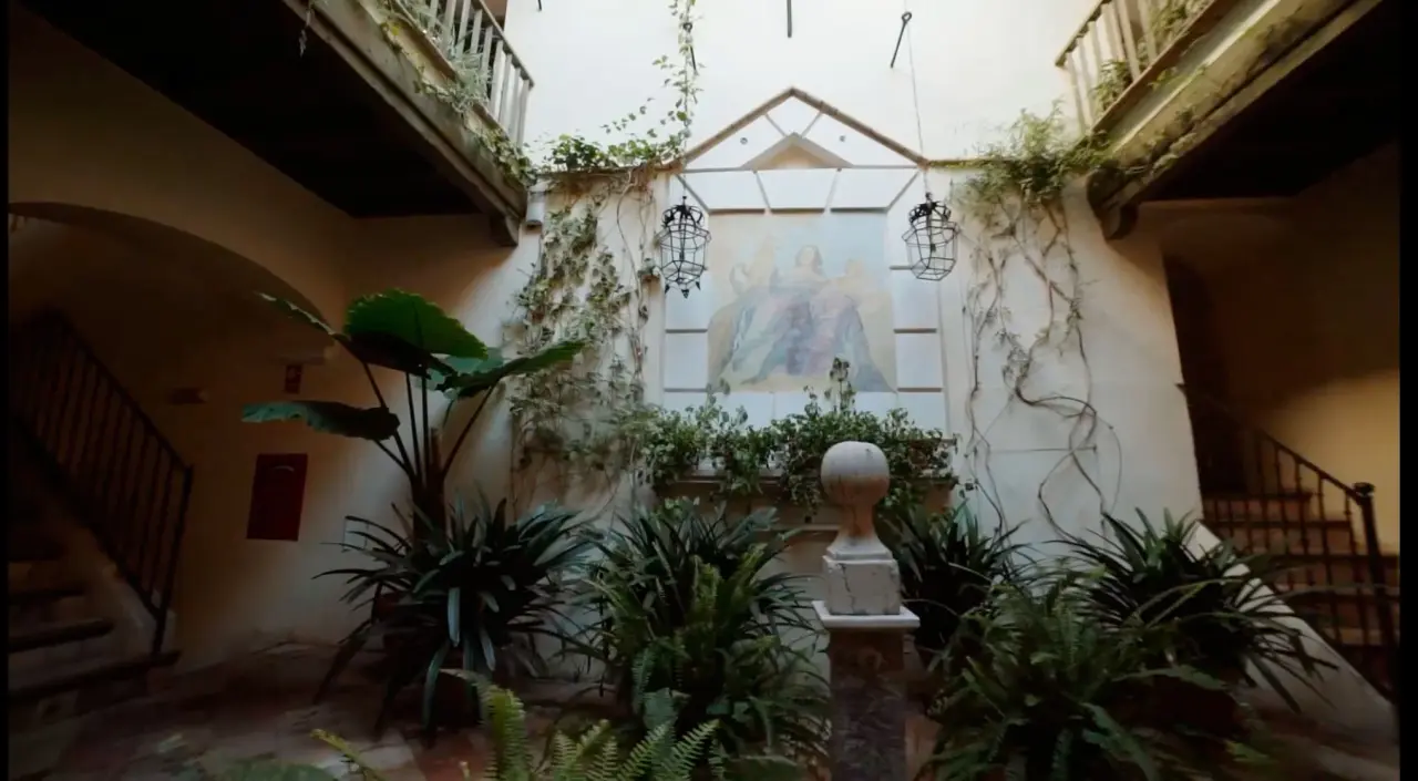 Patio interior de un edificio histórico con paredes blancas cubiertas de enredaderas, plantas verdes en el suelo
