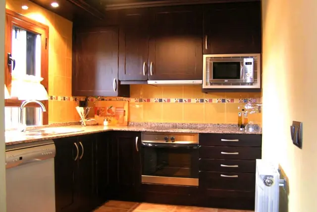 Cocina interior con muebles oscuros, encimera de granito, horno, microondas, fregadero y ventana.