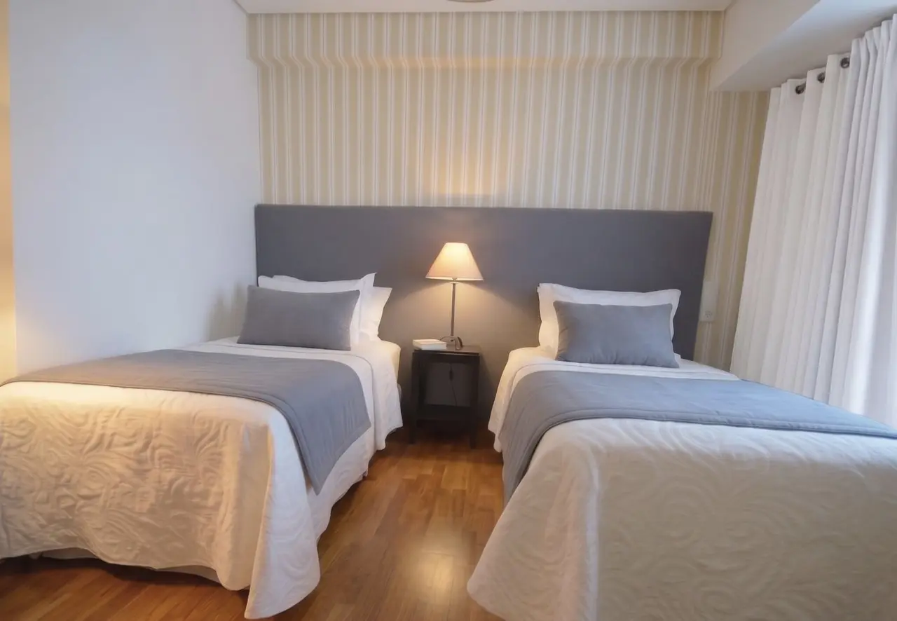 Habitación con dos camas individuales separadas, cada una con edredón blanco y cojines grises, cabecero gris común