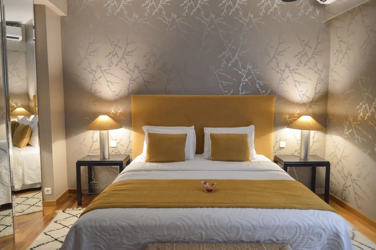 Habitación con cama king size vestida en tonos blanco y mostaza, cabecero amarillo, dos mesitas de noche con lámparas