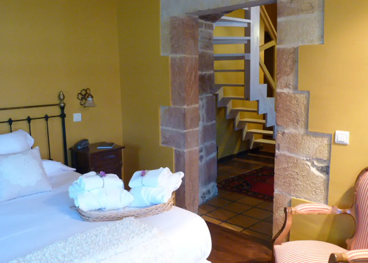 Habitación con cama, toallas en cesta y escalera de caracol al fondo.