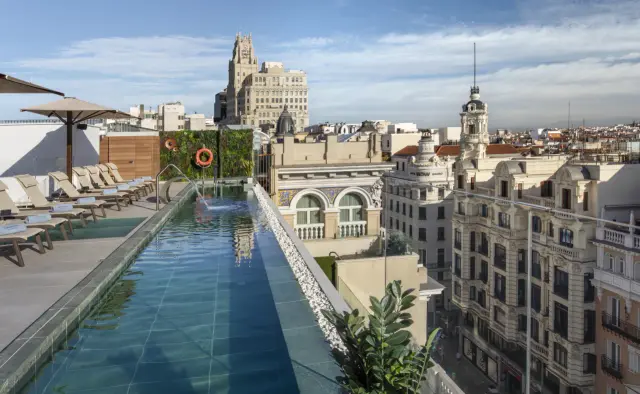Vista de una piscina infinita en la azotea de un hotel con tumbonas, sombrillas y vistas a los edificios históricos