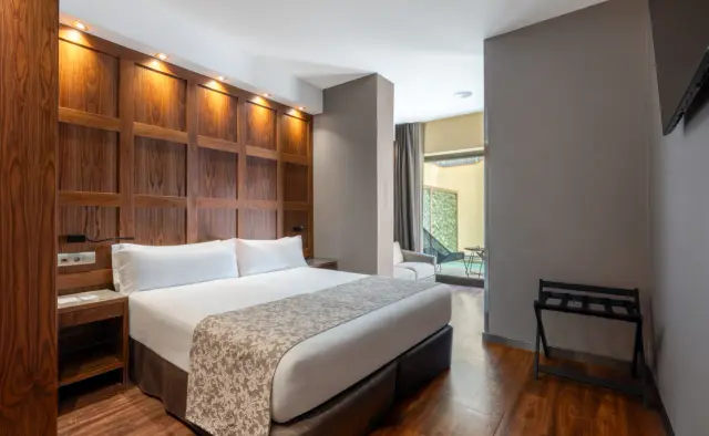 Vista de una habitación suite con cama king size, cabecero de madera iluminado, mesitas de noche, suelo de parquet
