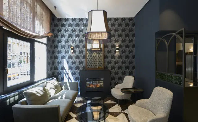Interior de una suite con chimenea moderna en el centro, sofá gris, dos sillones, mesa de centro redonda, suelo