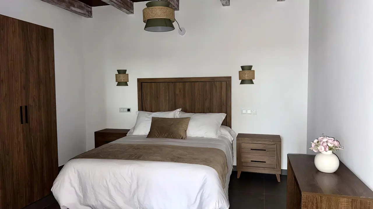 Habitación con cama doble, cabecero de madera, mesitas de noche, armario y decoración minimalista en tonos neutros.