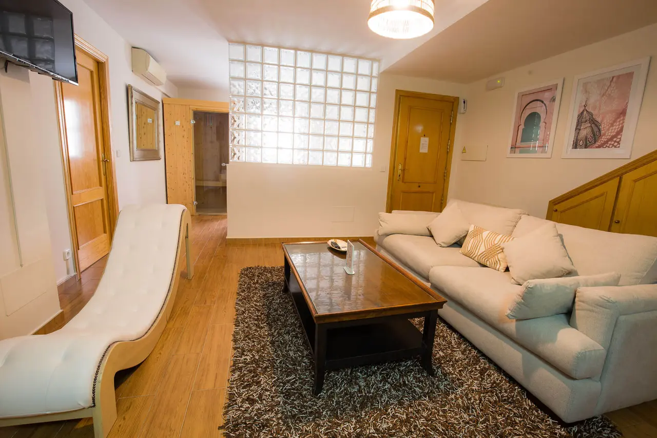 Sala de estar con sofá claro en forma de L, mesa de centro de madera oscura sobre una alfombra de pelo largo, chaise