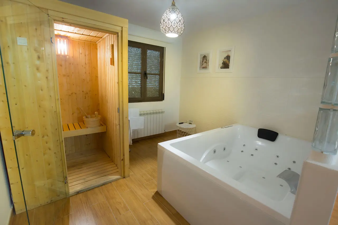 Habitación con spa privado que incluye una bañera de hidromasaje blanca y una sauna de madera con puerta de vidrio