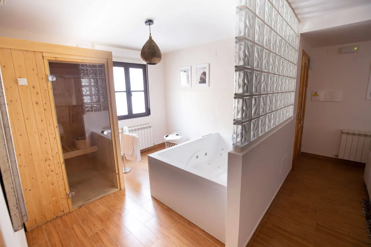 Habitación con spa privado que incluye una bañera de hidromasaje blanca rectangular, una sauna de madera con puerta