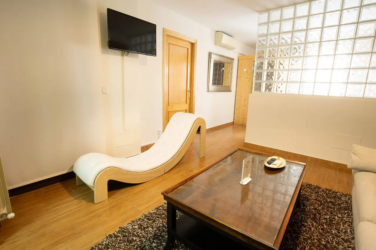 Interior de una habitación con suelo de madera, una chaise longue blanca curvada, mesa de centro de madera