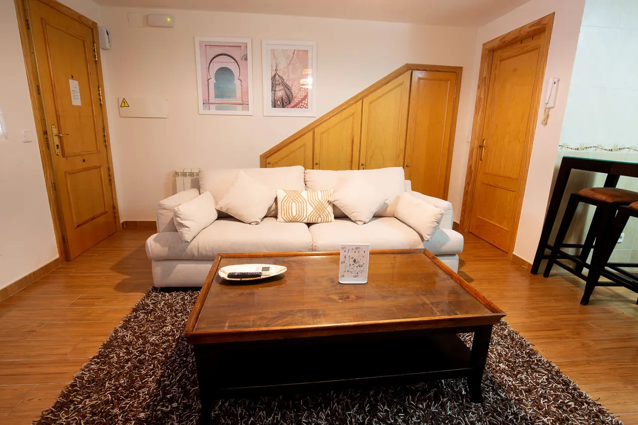 Sala de estar con sofá blanco de tres plazas, mesa de centro de madera oscura sobre una alfombra marrón, dos puertas