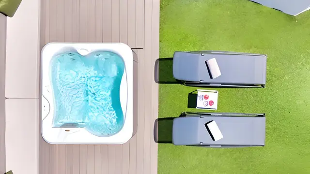Vista aérea de un jacuzzi con agua azul en terraza de madera junto a dos tumbonas en césped.