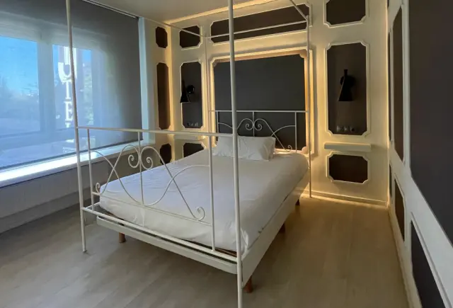 Habitación de hotel con cama de matrimonio de estilo antiguo con estructura metálica blanca, dosel y doselera, situada