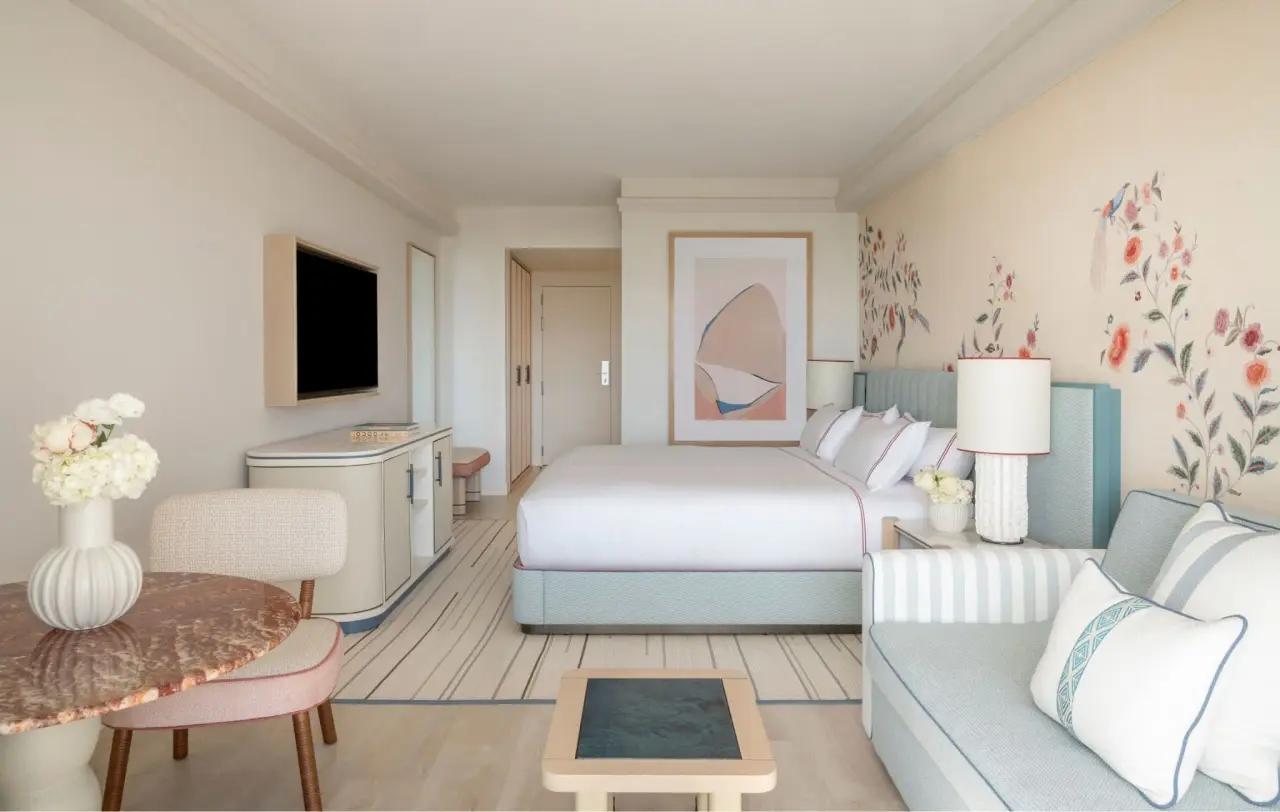 Vista de una suite de hotel con cama king size, sofá, mesa redonda con sillas, televisor en la pared, escritorio