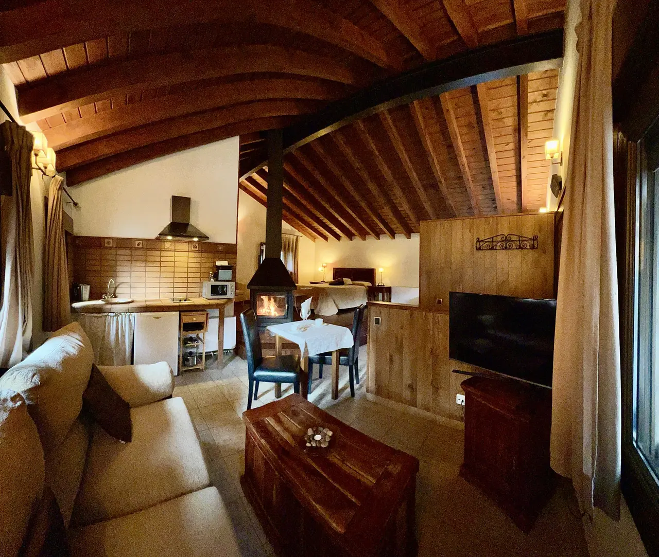 Interior de una cabaña rústica con techo de vigas de madera, sala de estar con sofá beige y mesa de centro de madera