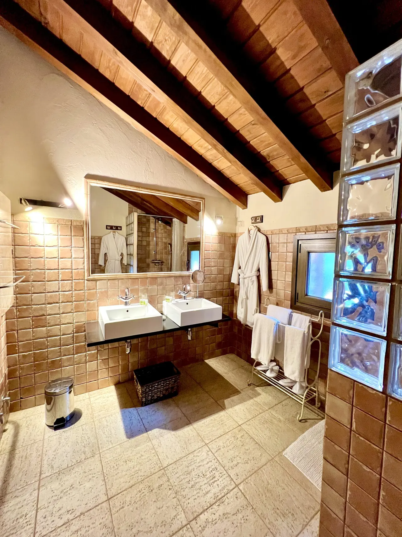 Baño con dos lavabos cuadrados blancos sobre un mueble negro, gran espejo rectangular, toallero con albornoces