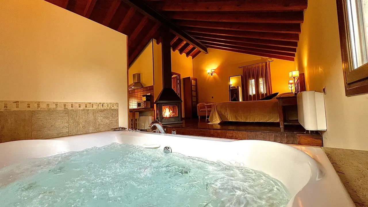 Jacuzzi para dos con agua burbujeante en primer plano, dentro de una cabaña rústica con techo de vigas de madera