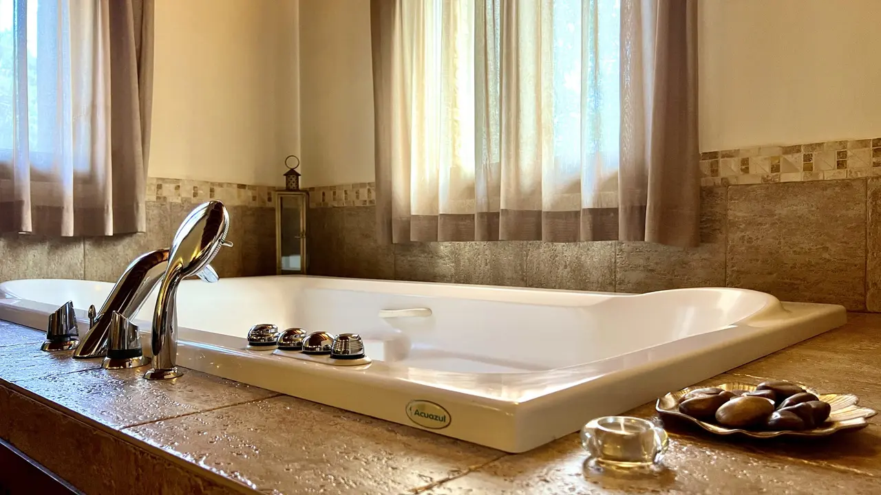 Jacuzzi rectangular blanco empotrado en encimera de piedra, con grifería cromada, mandos de hidromasaje y ventana