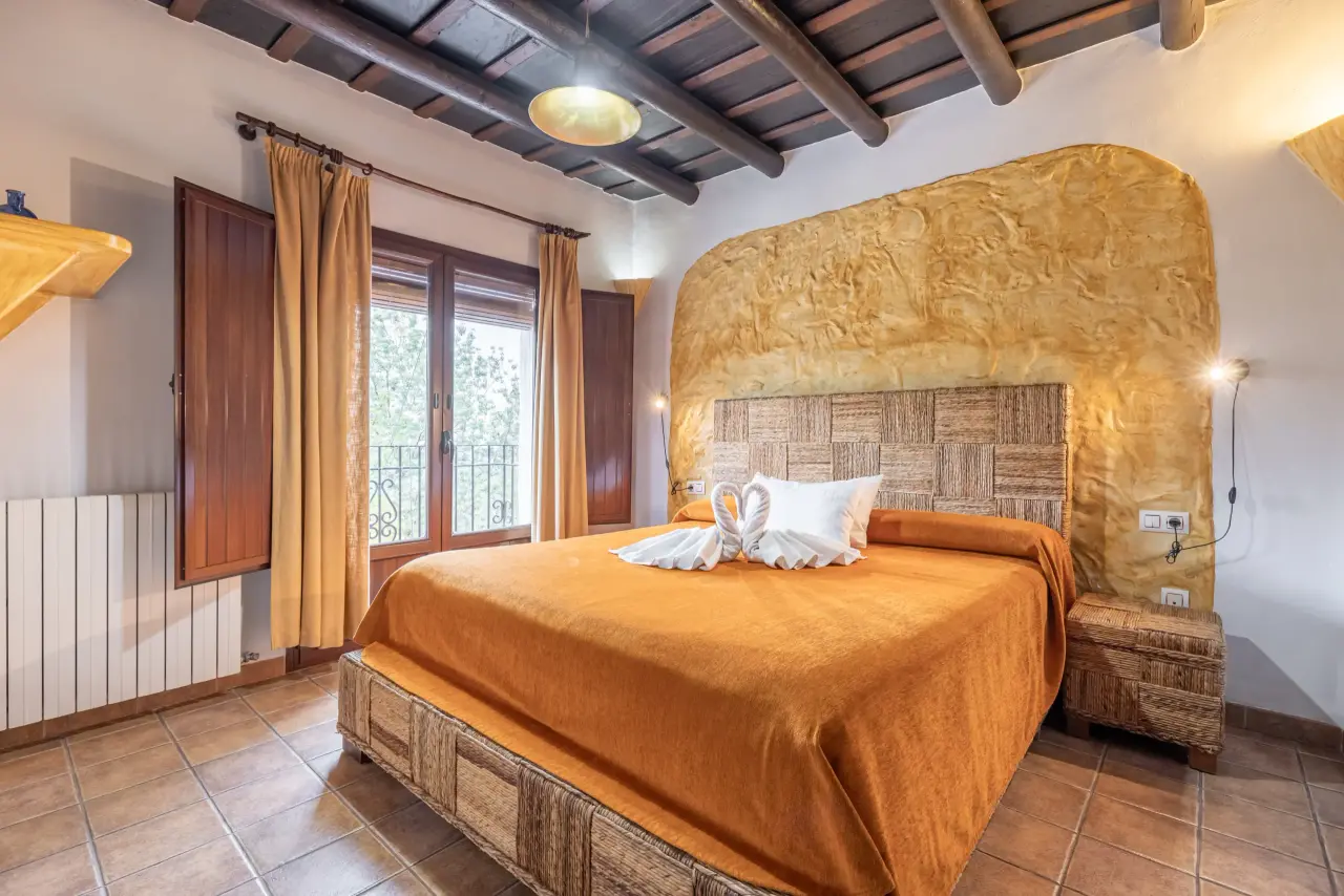 Habitación doble con cama grande vestida en tonos naranjas, cabecero de pared texturizado en amarillo, dos toallas