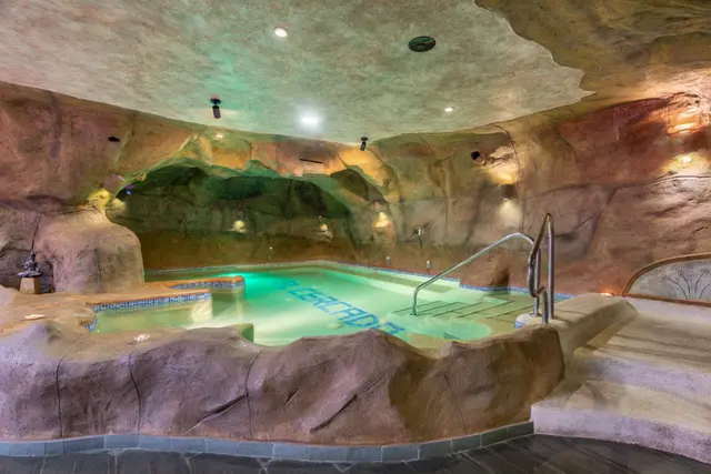 Vista de un spa privado con piscina interior iluminada en tonos verdes y azules, rodeada de paredes y techo simulando