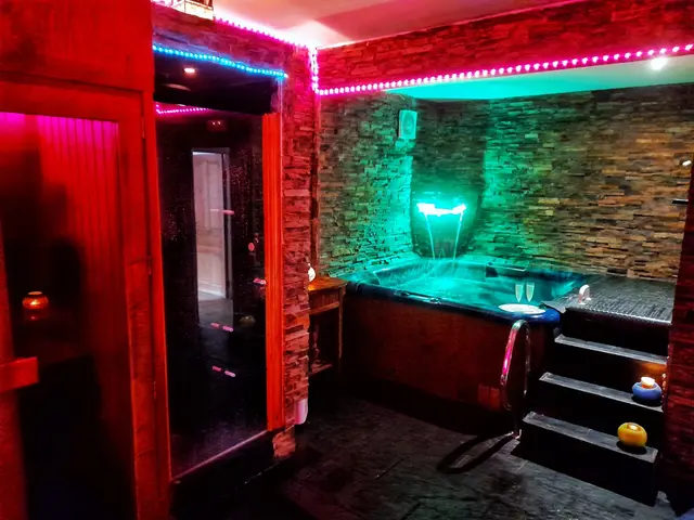 El Huerto del Abuelo: Spa privado con jacuzzi iluminado en tonos verdes y rojos, cascada de agua y paredes de piedra.