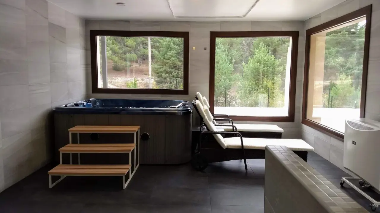 Interior de un spa privado con jacuzzi rectangular empotrado en el suelo, dos tumbonas reclinables con cojines claros