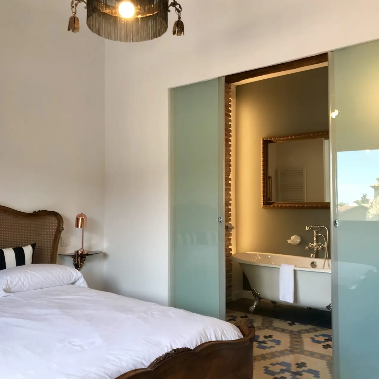 Vista de una suite con cama de madera y dosel en primer plano, y al fondo un baño separado por puertas correderas