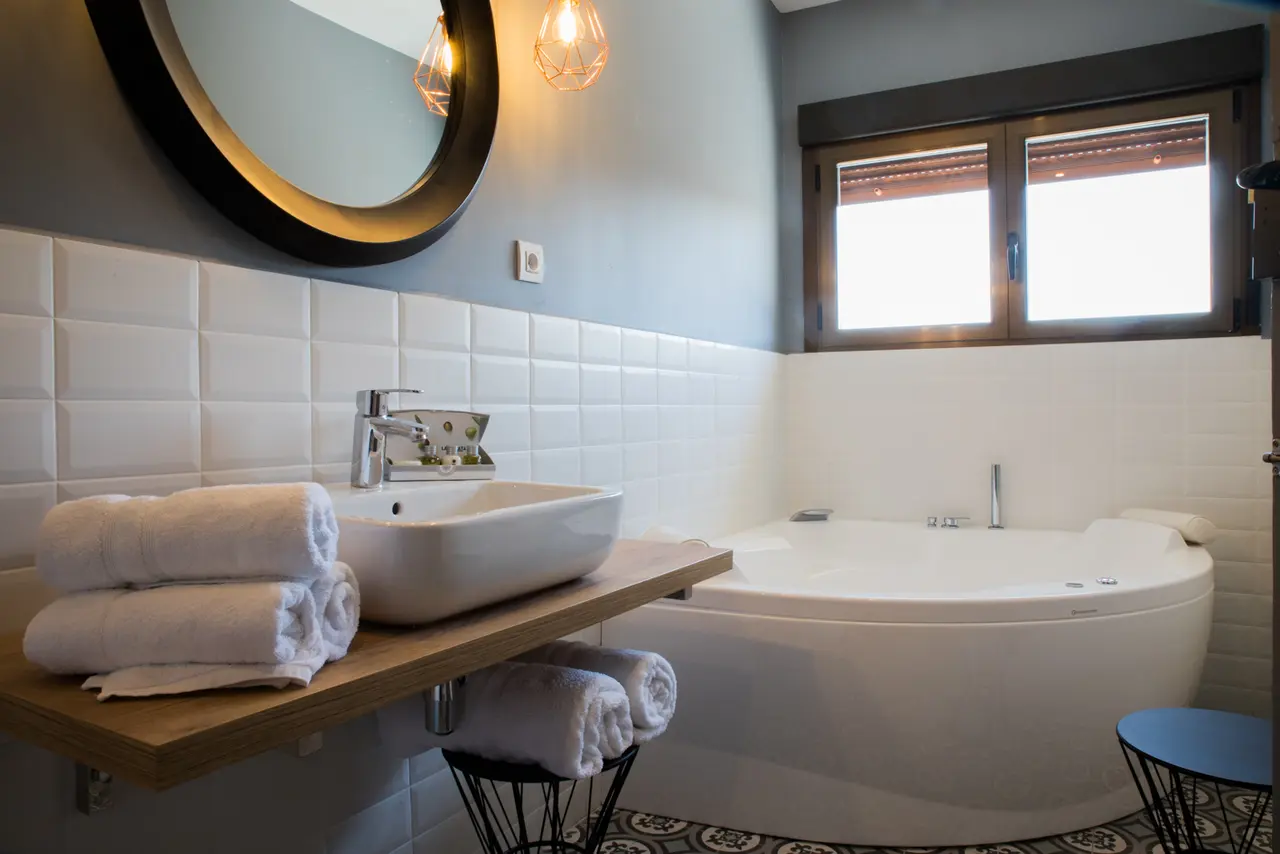 Baño con paredes de azulejos blancos, lavabo rectangular blanco sobre encimera de madera, grifo cromado, toallas