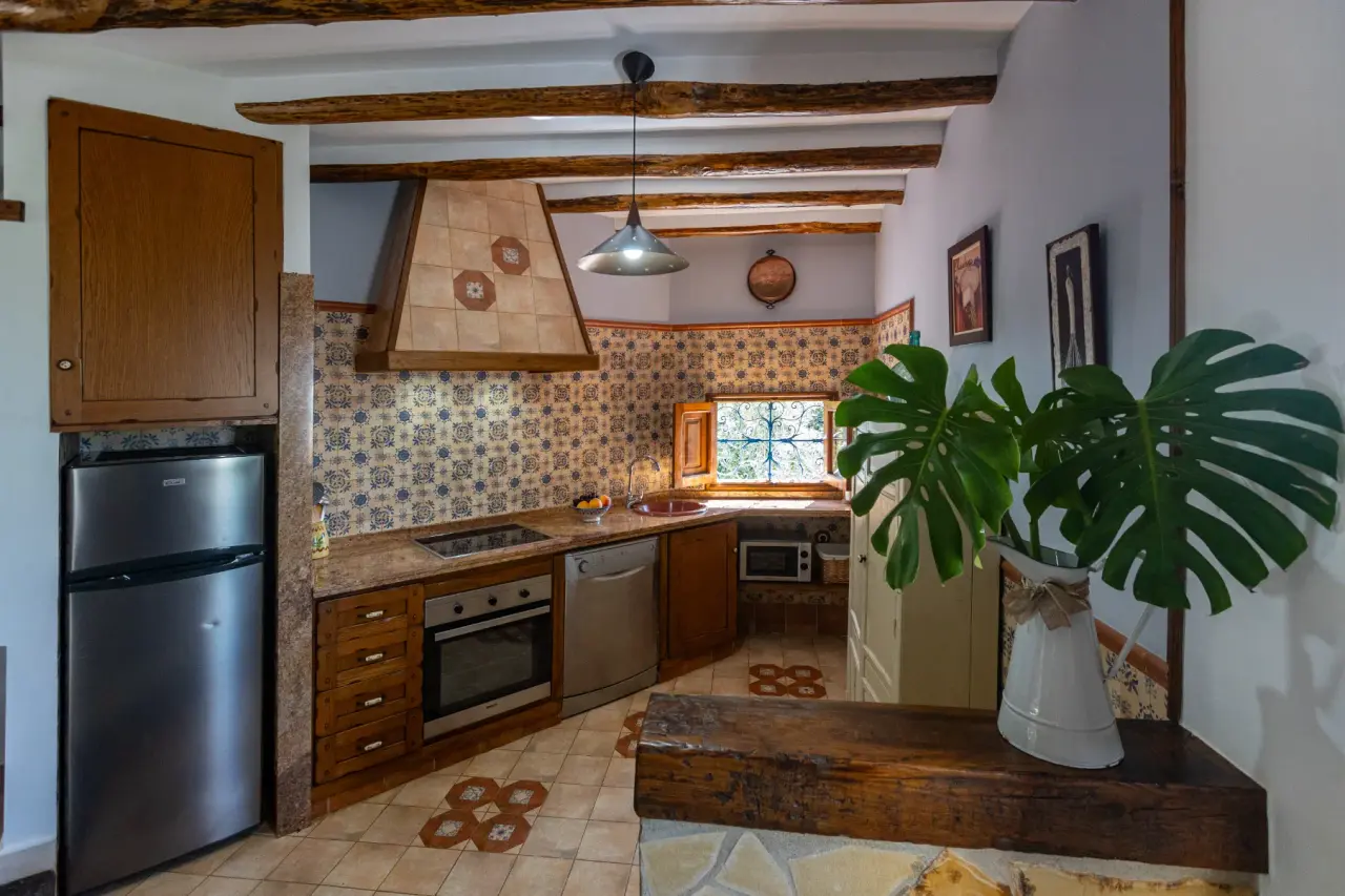 Cocina rústica con muebles de madera, electrodomésticos, encimera de piedra y vigas vistas en el techo.