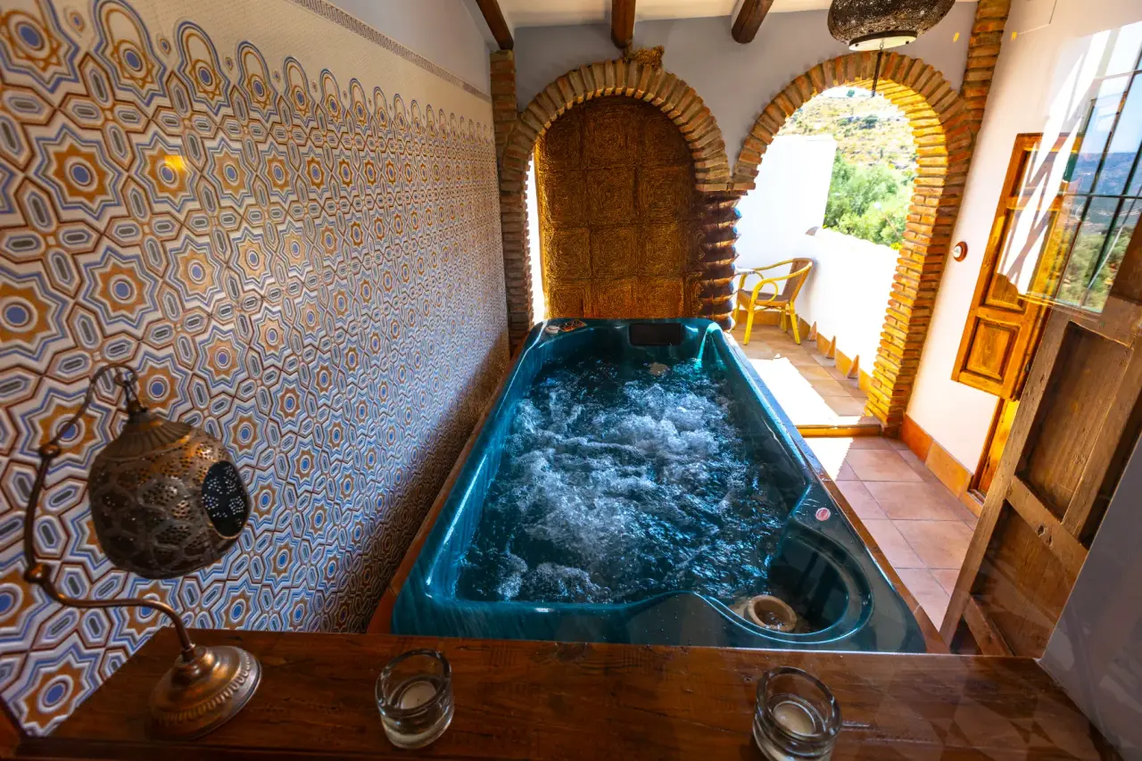 Jacuzzi privado con agua burbujeante en una terraza con arcos de ladrillo y vistas al exterior.