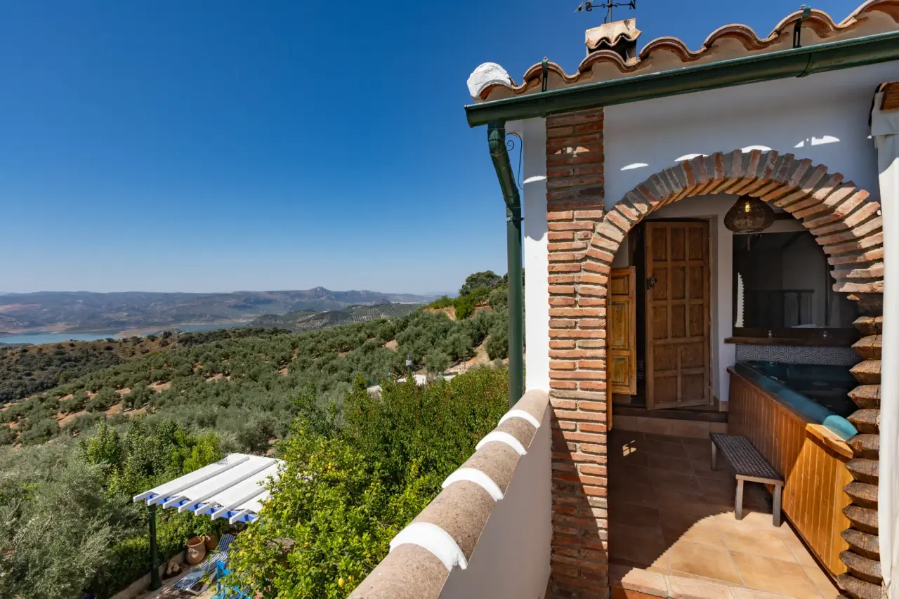 Terraza con jacuzzi privado junto a un arco de ladrillo y vistas panorámicas al valle y embalse.