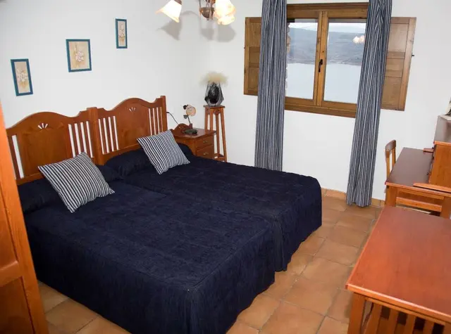 Habitación con dos camas individuales unidas, colcha azul marino, cabecero de madera, mesita de noche, ventana