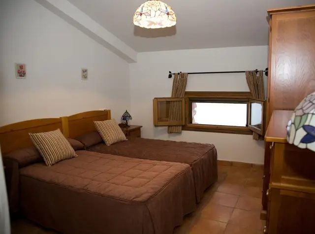Habitación con dos camas individuales unidas, colchas marrones, cabeceros de madera, ventana con cortinas a rayas