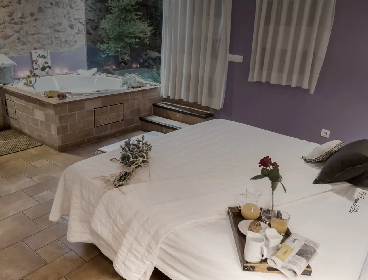 Vista de una habitación con una cama grande vestida de blanco y un jacuzzi empotrado en una plataforma de obra vista