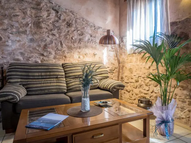 Interior de una habitación con sofá de rayas, mesa de centro de madera, lámpara de pie, pared de piedra rústica