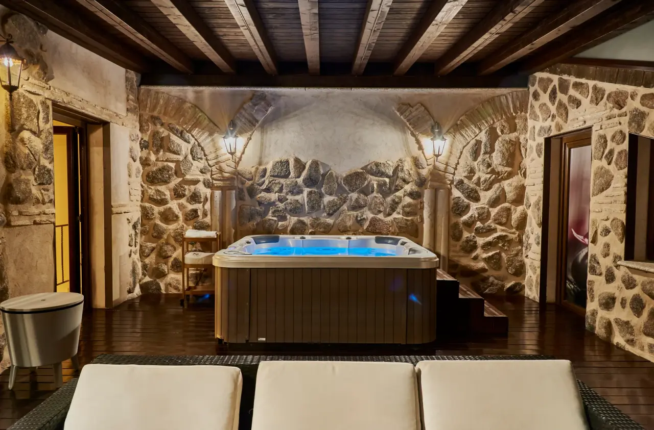 Jacuzzi privado rectangular con agua iluminada en azul, instalado en una sala rústica con paredes de piedra, arcos