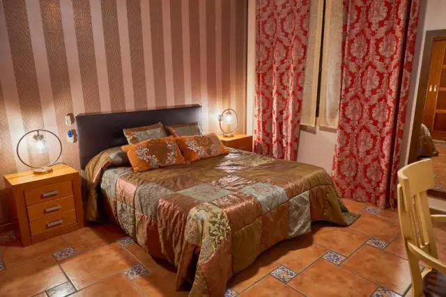 Habitación con cama doble, cabecero oscuro, mesitas de noche con lámparas encendidas, suelo de terracota con detalles