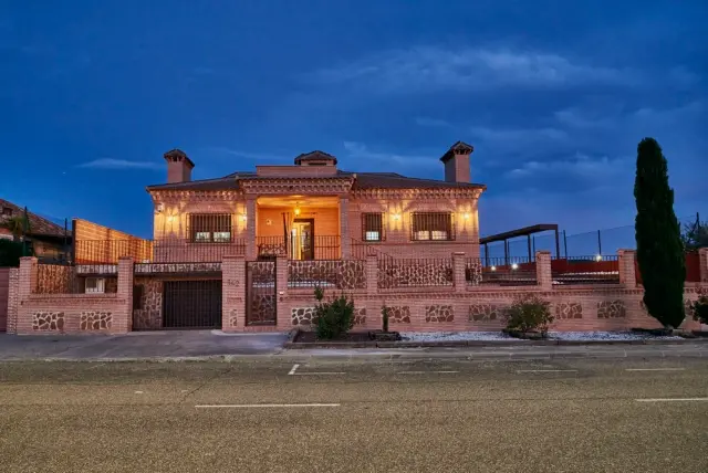 Vista frontal de una casa rural de dos plantas construida en ladrillo visto y piedra, con porche iluminado