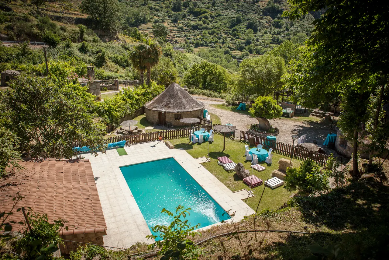 Vista aérea de una piscina rectangular con agua turquesa en un jardín rodeado de vegetación, con una cabaña circular