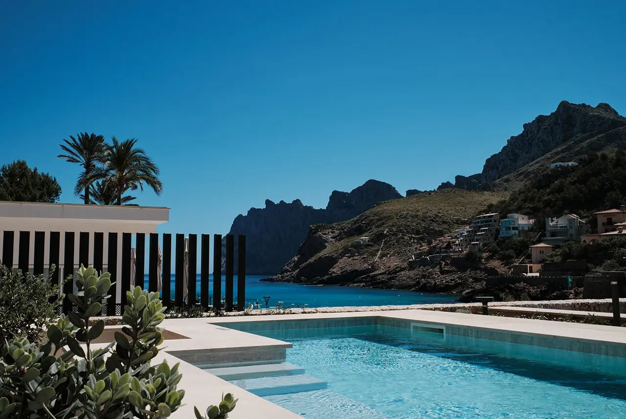 Piscina rectangular de agua turquesa con escalones de acceso, rodeada de una terraza de piedra clara.