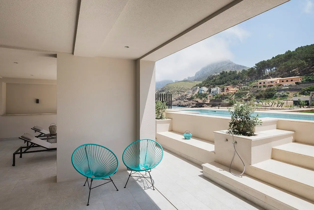 Terraza exterior de suite con dos sillas acapulco turquesa, zona de piscina privada rectangular al fondo y vistas