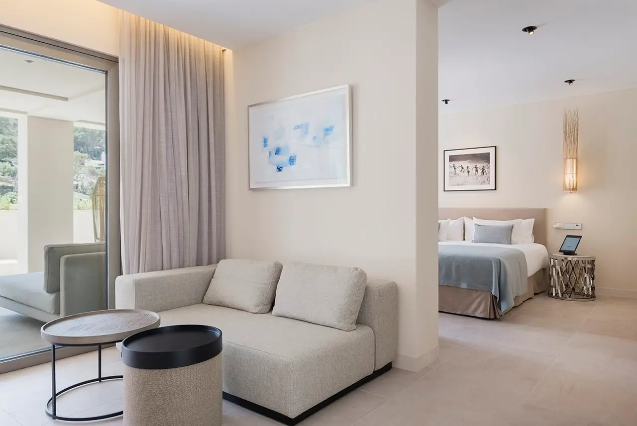 Interior de una suite con zona de salón que incluye un sofá beige, mesa de centro y acceso a terraza a través