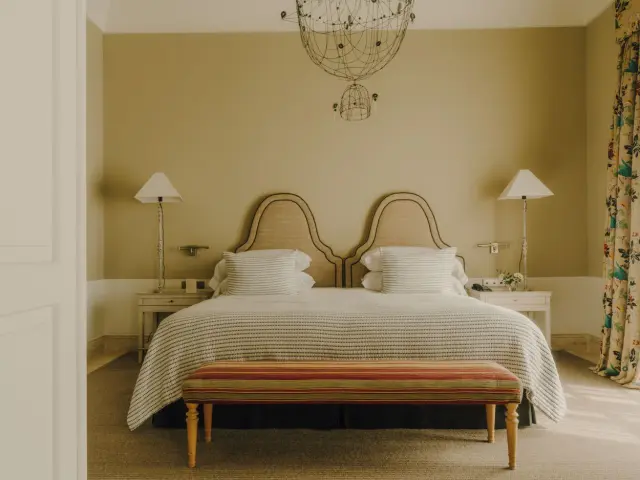 Vista de una habitación con una cama grande de matrimonio con cabecero doble curvado, cubierta con una colcha a rayas
