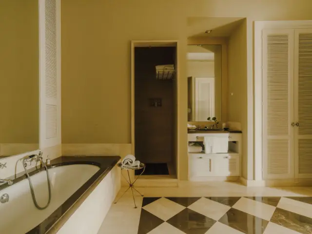 Interior de un baño con una bañera blanca empotrada en el lado izquierdo, suelo de damero en blanco y negro